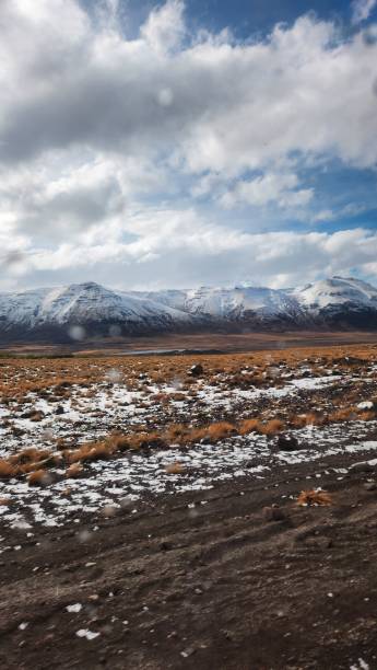 winter landscape in Argentine Patagonia, dirt road in the foreground with vegetation, dry pastures with snow around and mountain ranges in the background, with blue sky with clouds stock photo