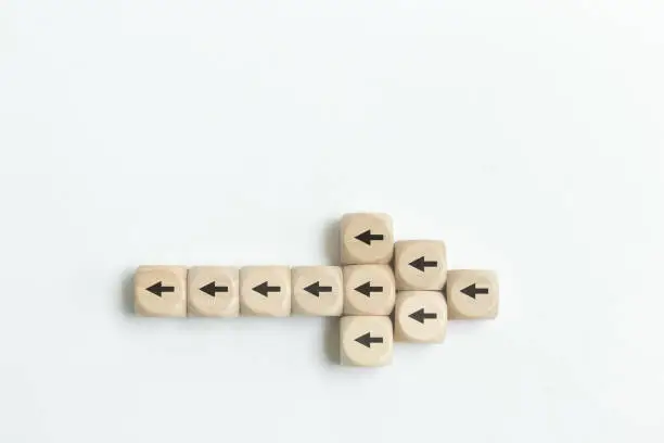 Arrow icon on wooden cubes with little arrow icons pointing opposite direction. Resistance to change in business concept.