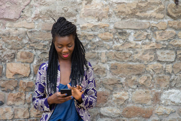 istock Portrait of an African woman with dreadlocks smiling while using smartphone touchscreen outdoors in town. 1501984681