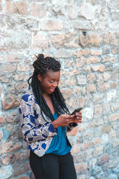 istock Portrait of an African woman with dreadlocks smiling while using smartphone touchscreen outdoors in town. 1501984683