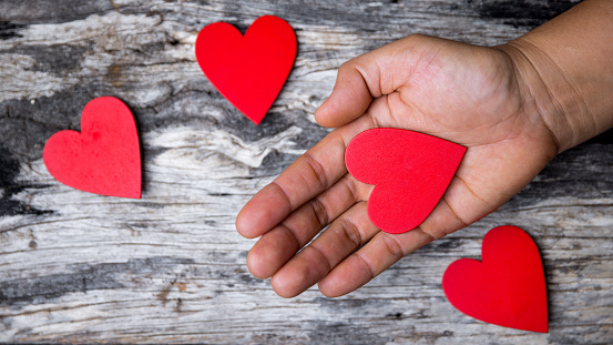 The red heart is on hand that showing love to another person. Heart is the symbol of showing love, cares, charity, help and compassion. People in the families and communities love each other.