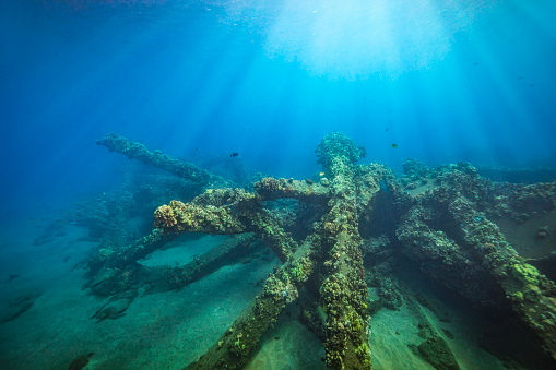 Light rays shining on sunken old wharf wreck and debris on the ocean floor with clear blue water.