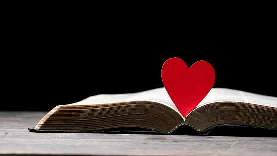 The red heart on holy bible book is the symbol of love from God. The God gives love to all people. We can see or find bible at the church. The bible is the in Christianity religion. Two heart on page.