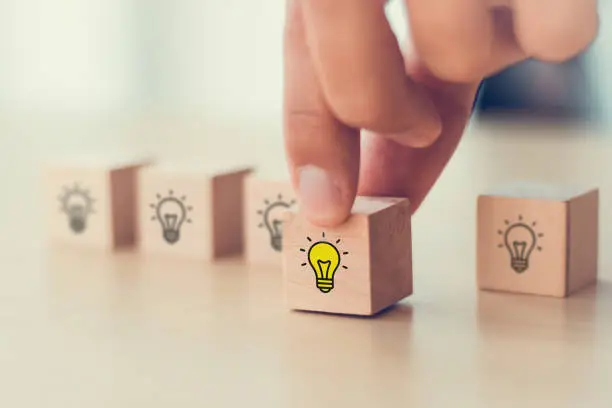 Creative idea, solution and innovation concept. Idea generation and screening for product development process. Wooden blocks with light bulb and yellow color icons on clean background and copy space.