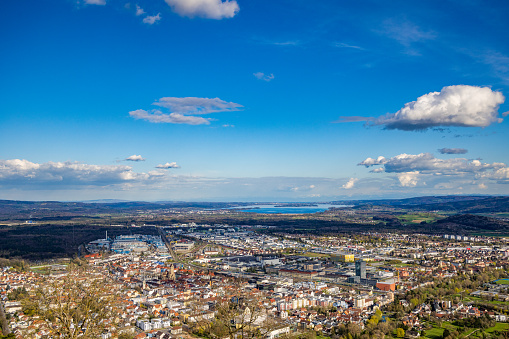 Bird's-eye view of the modern densely populated European industrial city of Singen, green mountains and wooded hills against the backdrop of the blue Lake Constance and cloudy sky