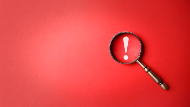 Magnifier magnifying exclamation mark on red background. Alert and precaution concept. Caution and risk management security signal announcement hazard and dangerous notice symbol stock photo