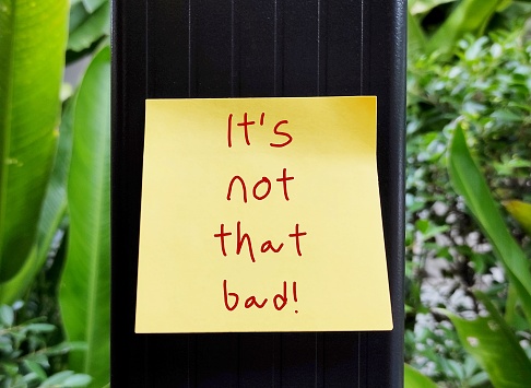 Yellow note stick on post with handwritten text ITS NOT THAT BAD!, self talk or encouragement message to cheer up - to become less sad or to make someone feel less sad