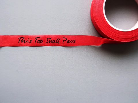 Red tape on gray copy space background with handwritten text THIS TOO SHALL PASS, to remind self that nothing, no matter good or bad wonderful or horrible, lasts forever - current situation or feeling will pass
