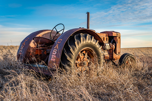 Coderre, SK- April 9, 2020: Sunburst at sunset over a vintage Case tractor abandoned in tall grass on the prairies in Saskatchewan