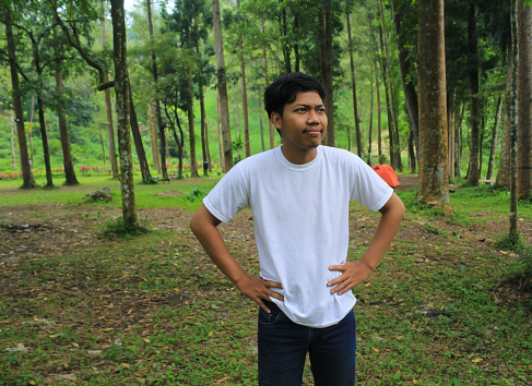 young asian man is angry with hands on waist when have holiday trip in tropical forest looking away. young asian man wearing white t shirt