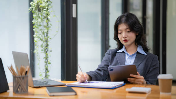 istock Attractive business Asian woman using a digital tablet while sitting at a workplace desk in an office. 1502099928
