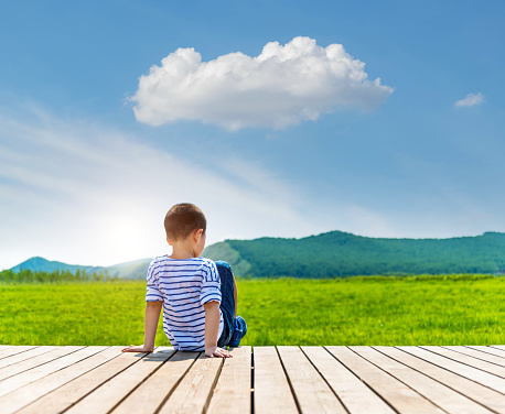 Little boy sitting on wooden sidewalk