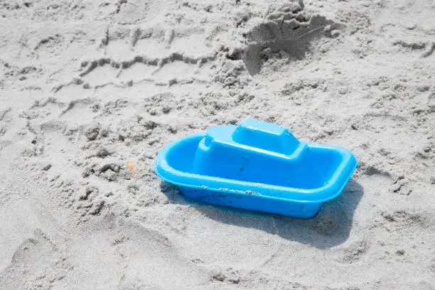 abandoned blue toy boat on the sand at the beach, not being played with, copy space