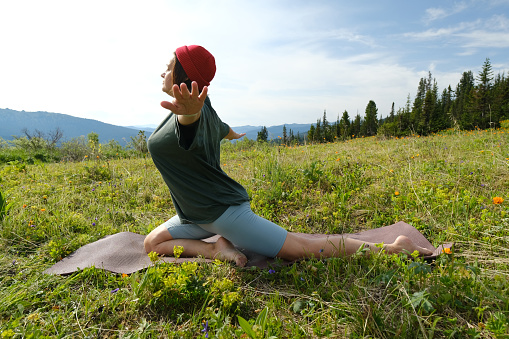 Female  doing yoga, meditation and sun salutation on blossom meadow and mountains background. Morning healthy activity.
