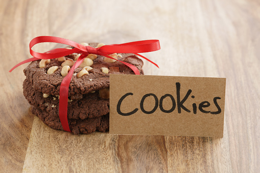 stack of homemade chocolate cookies with hazelnuts tied with ribbon on wood table and paper card, shallow focus