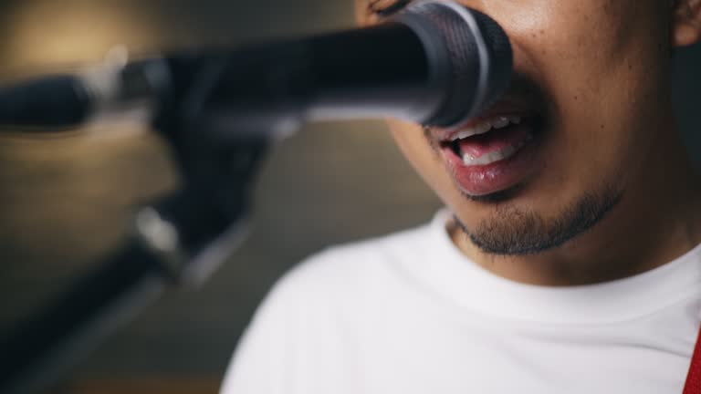 Asian male musicians in casual clothes playing electric guitar while vocalist singing song into microphone