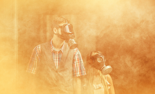 In this thought-provoking photograph, a young couple stands united against the backdrop of a heavy, foreboding orange smog. Their faces are concealed by protective gas masks, the only visible indication of their identity. The vibrant orange hue permeates the entire scene, creating an atmosphere of eerie uncertainty.  The air around them feels heavy and suffocating, emphasizing the urgency of the situation. The gas masks they wear serve as a stark reminder of the environmental challenges that humanity faces in an increasingly polluted world.