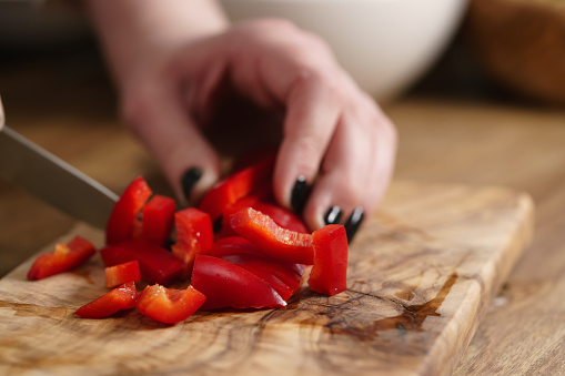 young female hands chopping red bell pepper on kitchen table, shallow focus