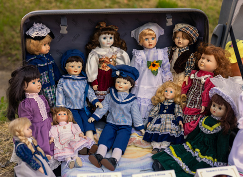 Heap of doll puppets wearing decorative costume in suitcase in flea market