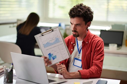 Marketing manager showing document with chart when video calling coworker from another department