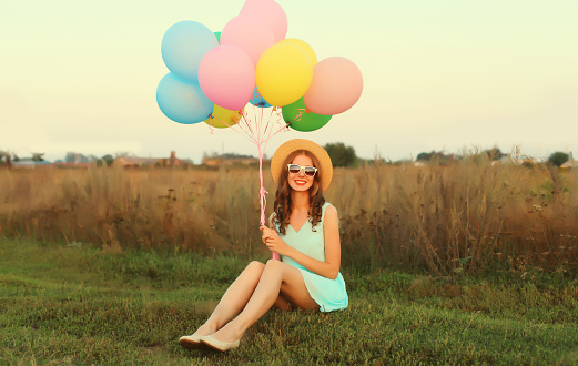 Happy cute smiling young woman with bunch of colorful balloons wearing dress outdoors