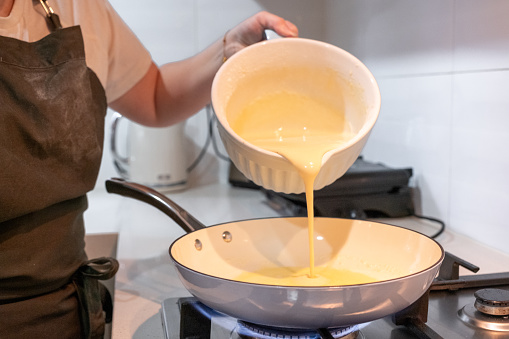 A girl pouring pancake mix into a hot pan