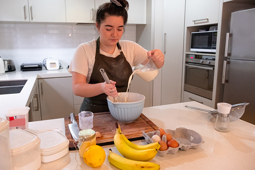 A girl in a home kitchen is mixing milk into the baking bowl