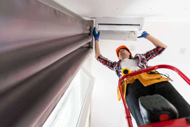 istock Worker installing or repairing air conditioner. Young man in uniform standing on ladder with toolbox and installing new air conditioner on wall. AC installation, maintenance and repair service concept 1502189216