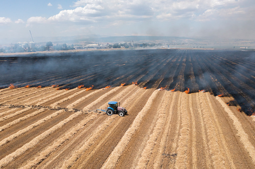 A farmer in his tractor cultivates the earth trying to contain a wheat field fire believed to be ignited by the harvester striking a rock.
