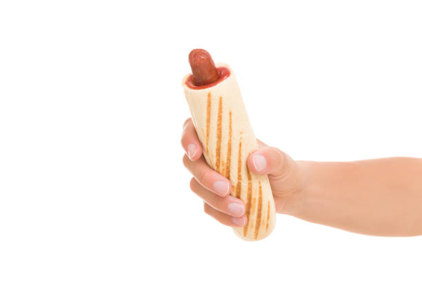 junge erwachsene frau hand hält frischen französischen hot dog mit rotem ketchup isoliert auf weißem hintergrund. closeup. fastfood. vorderansicht. - sausage grilled isolated single object stock-fotos und bilder