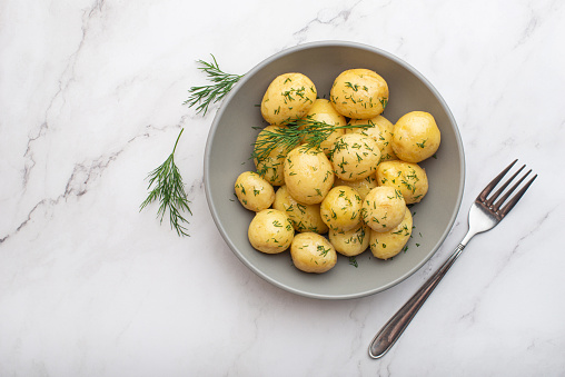 Young potatoes with butter and dill in a gray plate on a white background