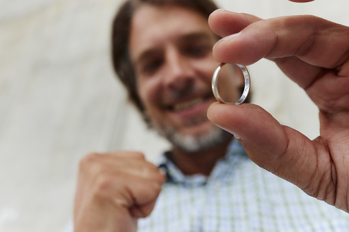 Close up of happy man holding a wedding ring and celebrating his future marriage.