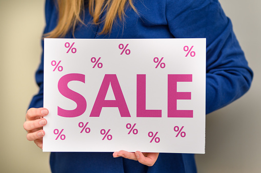 A woman holding a card with a pink sale sale inscription, closeup