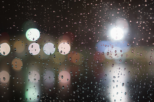 closeup of raindrops on window in night with lights, shallow focus