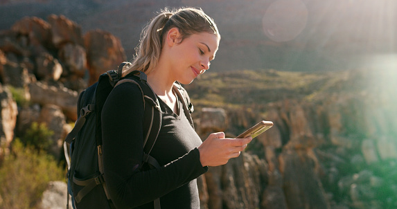 Woman, hiking and search for direction with phone in mountains, adventure or fitness with smile in summer. Happy hiker girl, smartphone and texting on social media app, journey or workout in sunshine