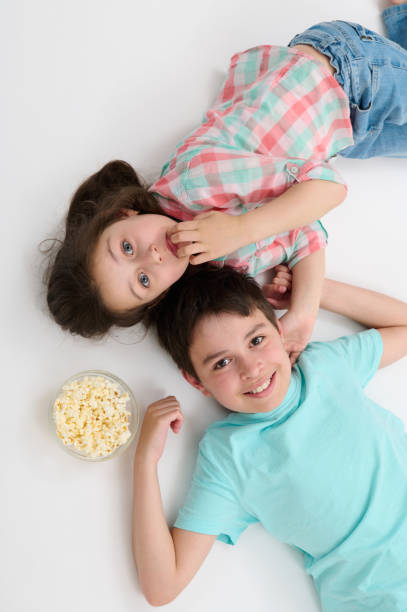 istock Top view happy kids smiling looking at camera, lying on their backs on white background near a bowl with tasty popcorn 1502220492