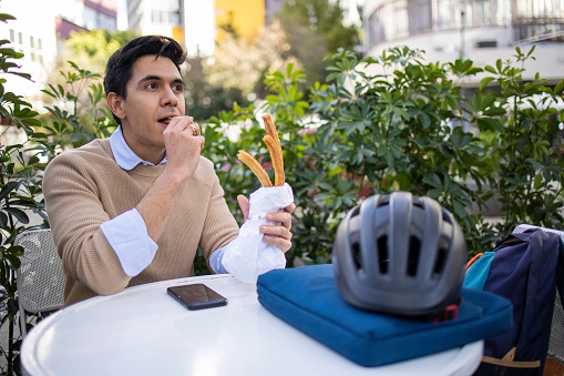 Young man sitting at cafe and eating fresh churrose