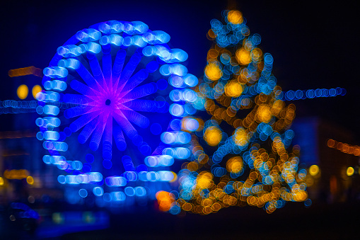 Defocused view of illuminated Christmas tree and Ferris wheel with abstract bokeh lights at night