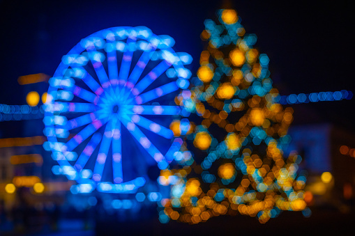 Defocused view of illuminated Christmas tree and Ferris wheel with abstract bokeh lights at night