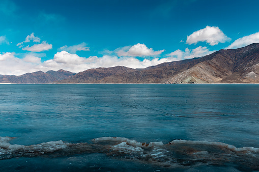 Nature's Frozen Jewel: Pangong Lake's Captivating Winter Scene, frozen blue water surface with cracks, snowcapped mountain in distance