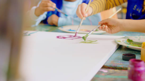 istock Closeup, hands and students painting, classroom and education with fun, artwork and creativity. Zoom, children and kids with fantasy, craft or youth with watercolor, brushes or relax with inspiration 1502226768