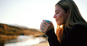 Woman, relax and camp coffee by a river in morning in summer by lake. Mockup, young female person and tea at sunrise on holiday, travel and vacation with hot drink and freedom from camping outdoor