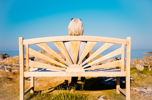 Woman sitting on a wooden bench lost in thought, looking out to the horizon. What can she see?