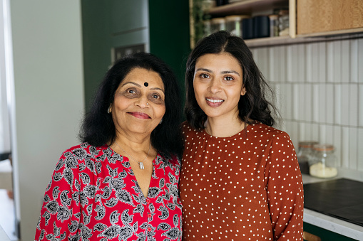 Waist-up portrait of Indian women in 40s and 60s dressed in casual clothing, standing side by side, smiling at camera.
