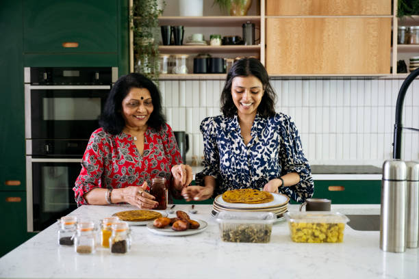 Cheerful Indian women preparing food in kitchen Waist-up view of casually dressed adults in 40s and 60s standing at counter and smiling while arranging chapati on plates for midday meal. indian wedding stock pictures, royalty-free photos & images