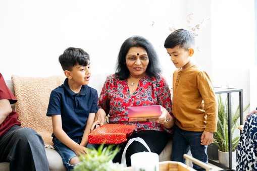 Casually dressed boys on each side of their smiling grandmother as she opens gift during family celebration at home.