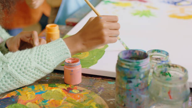 Closeup hands, child and painting with dip, container and classroom for learning, talent development and school. Kid artist, education and academy for inspiration, art or color for creativity at desk primer plano de manos, niño y pintura con inmersión, contenedor y aula para el aprendizaje, el desarrollo del talento y la escuela. artista infantil, educación y academia para la inspiración, el arte o el color para la creatividad en el escritorio