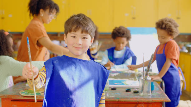 istock Boy, paintbrush and portrait in classroom with smile, learning and development with teacher, school kids or art. Young male child, happy and group for education, creativity and painting at academy 1502238651