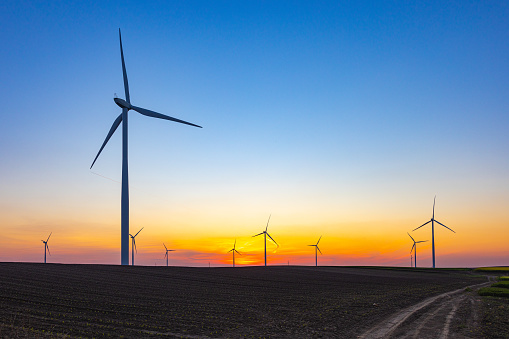 Horizontal axis wind turbines on agricultural field under the blue and golden sky at sundown, energy evolution and sustainability