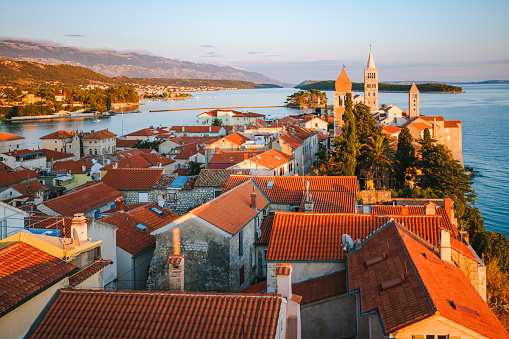 High angle view over orange colored tiled house roofs on towers and seascape, old town Rab on the island of Rab in Croatia